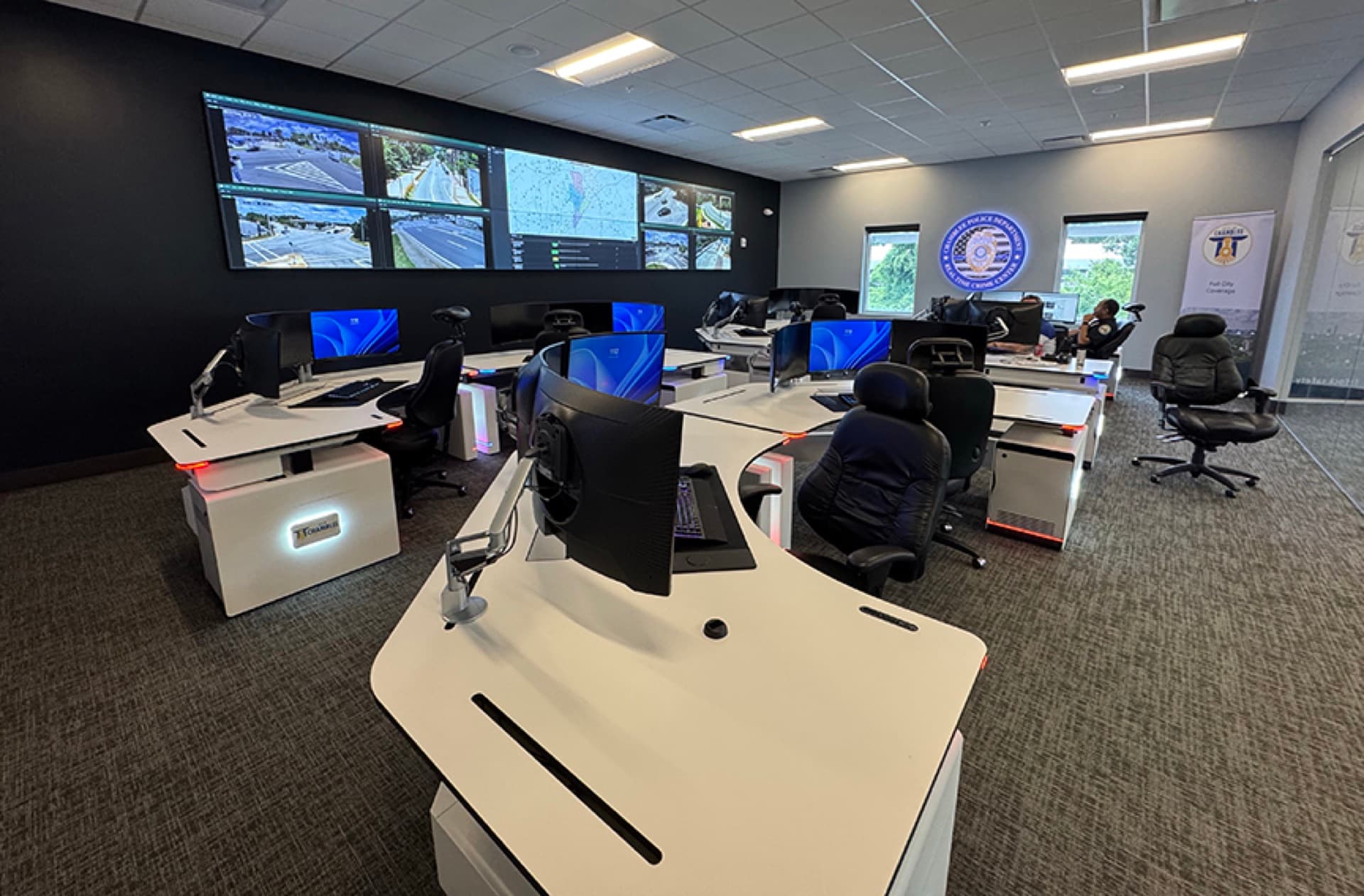 Chamblee Police real-time crime center with white 911 dispatch consoles facing a traffic-camera video wall